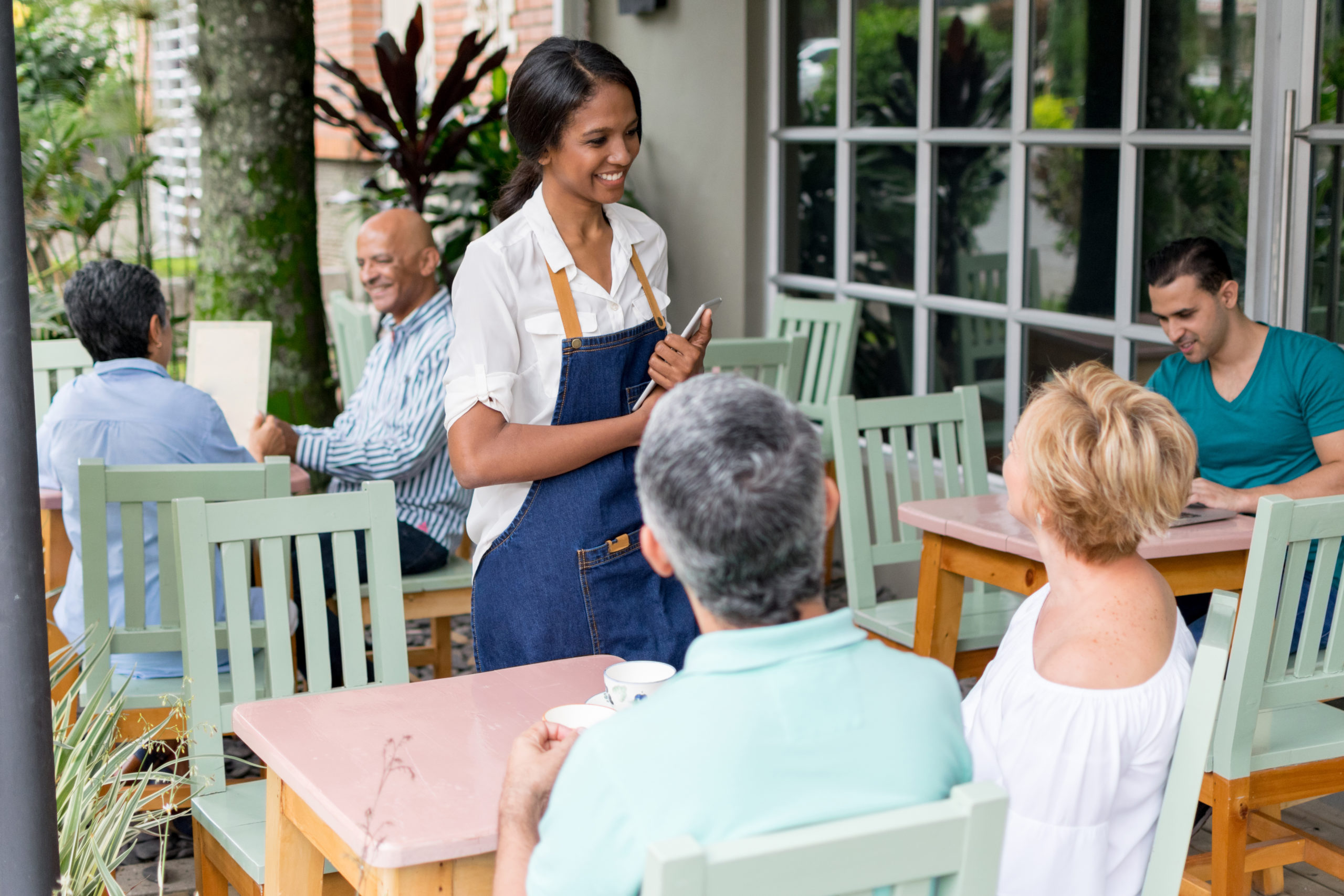 Friendly waitress taking the order from an adult couple while other customers sitting at the background smiling