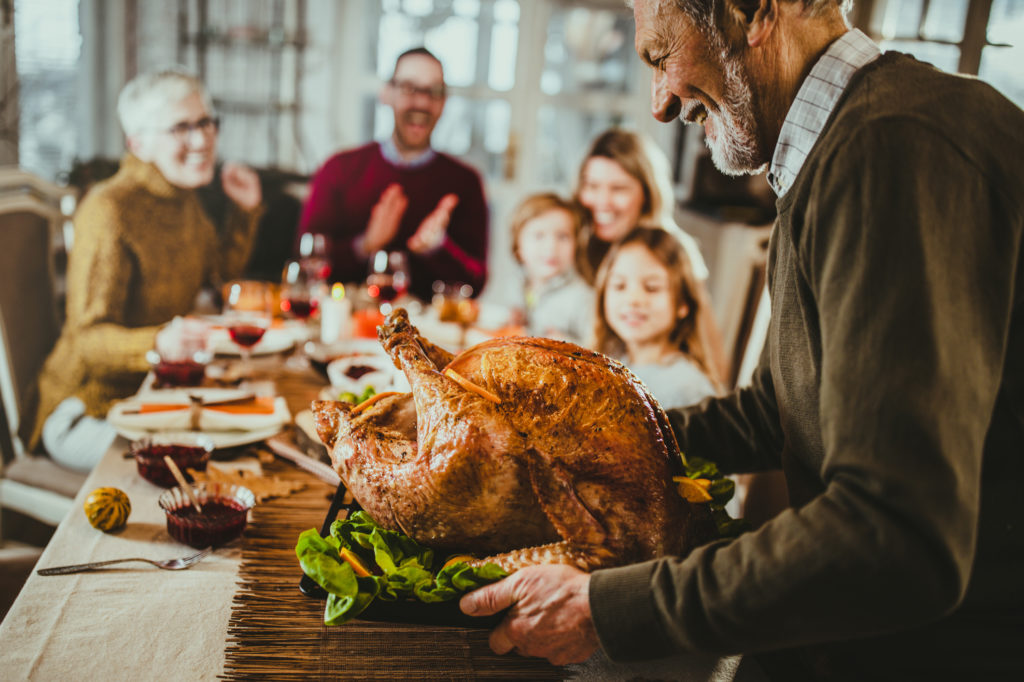 Thanksgiving dinner with family Happy senior man bringing Thanksgiving turkey to the table